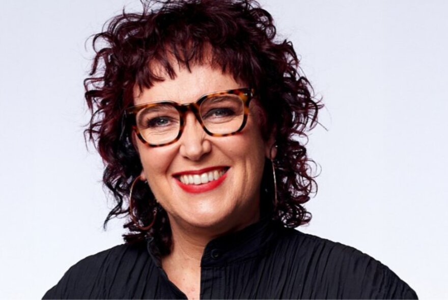 Portrait of journalist Natasha Mitchell, smiling, in front of a pale grey background.