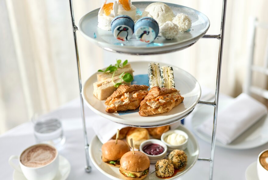 A three-tier afternoon tea plate wtih sliders and savoury treats at the bottom and Pingu-themed cakes at the top. 