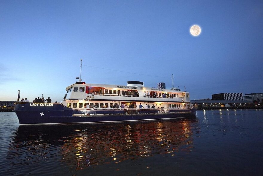 Cruise boat at night on the water under a full moon.