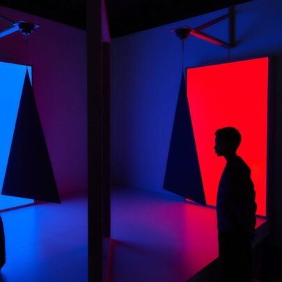 Dark silhouettes against panels of red and blue in a dark exhibition space.