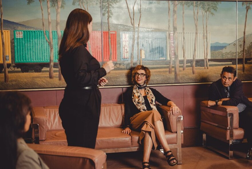 People seated on brown shiny sofas in a room with a mural of railroad cars in a country setting.