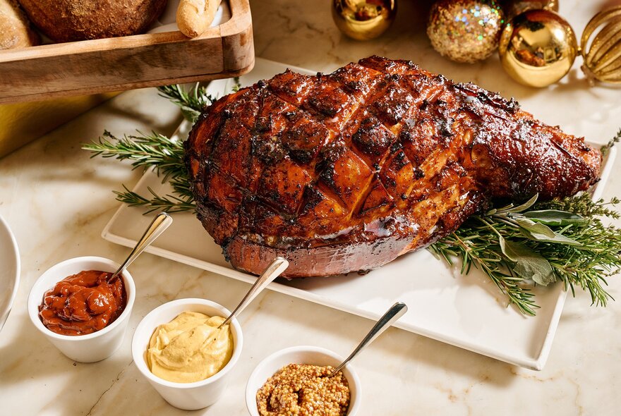 Christmas ham on a bed of rosemary with condiments.