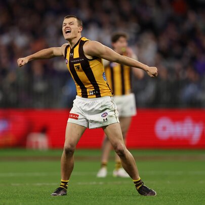 A Hawthorn football player looking exuberant with his arms out on a football field. 