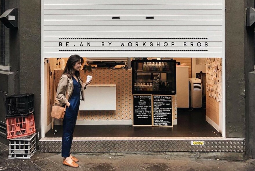 Cafe exterior with customer standing with takeaway coffee and glimpse of counter and blackboard menu.