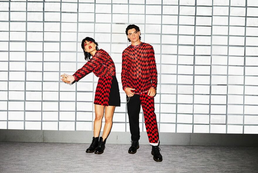 Two models in geometric red and black outfits, posing in front of a tiled wall