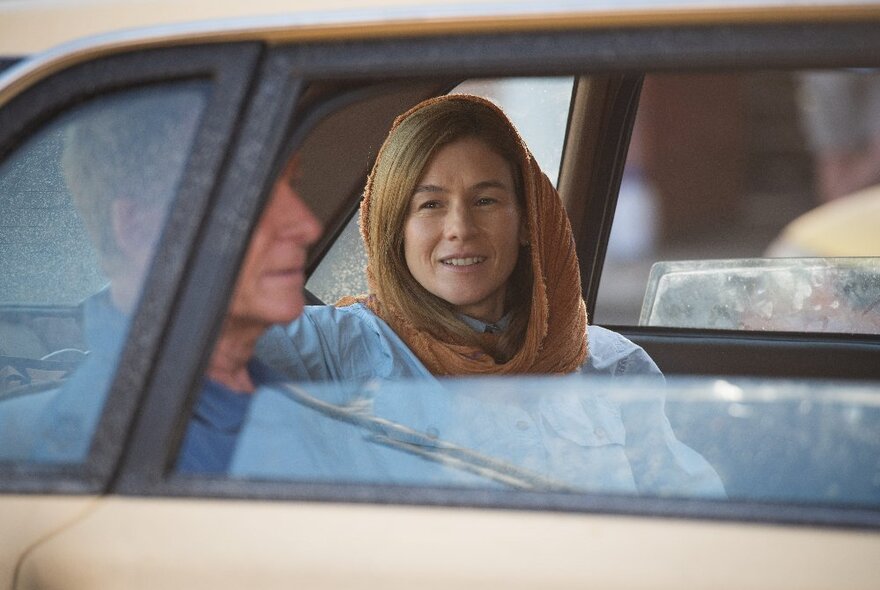 A still from the movie The Correspondent showing a woman in the back of a car with a headscarf.