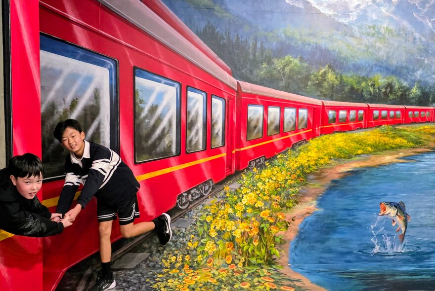 Two children engaging with a hand-painted interactive artwork of a red train inside ArtVo.