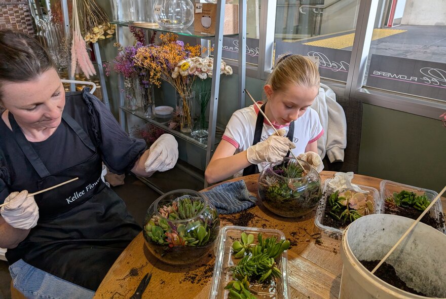 A woman and young girl in a workshop situation making terrariums. 
