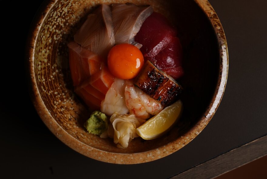 Looking down at a shallow bowl of slices of raw fish, with a raw egg yolk resting in the centre.