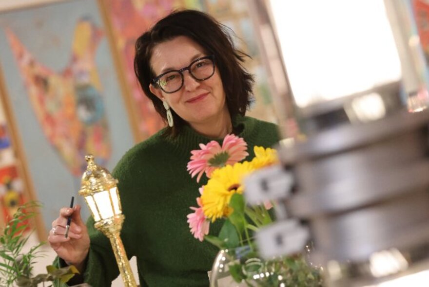 Tutor and teacher artist Debra Longin smiling and standing behind a vase of flowers.