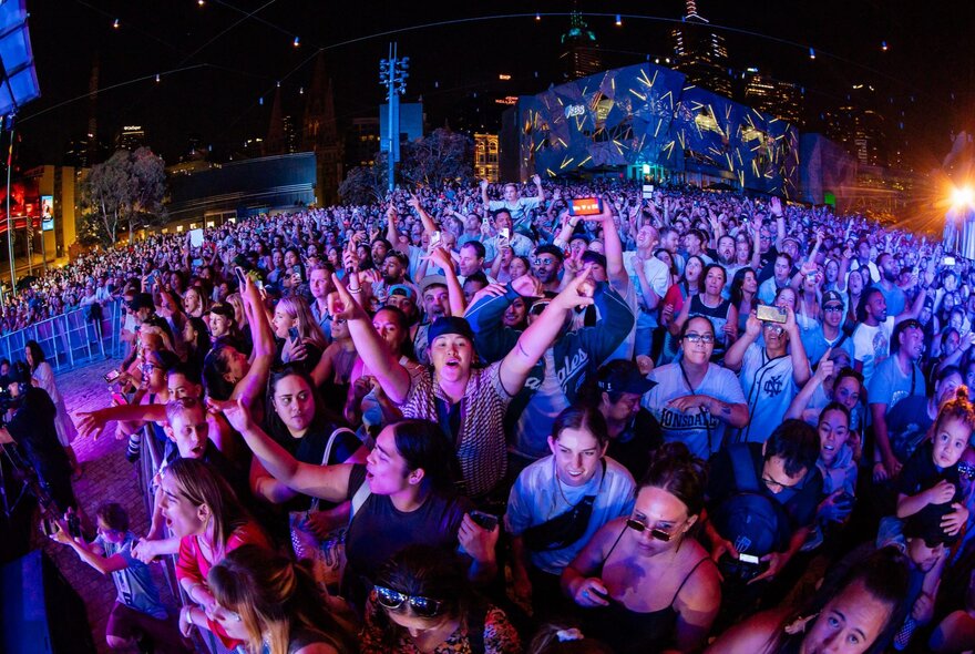 Crowds of people at Fed Square in front of the main stage, enjoying themselves and dancing at a music event.
