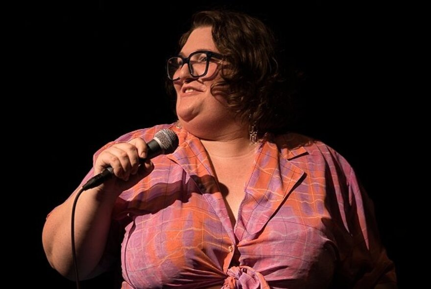 Large comedian smiling on stage, holding a microphone.