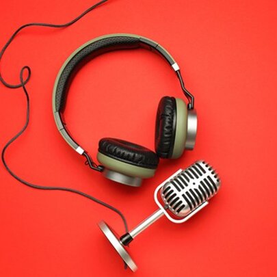 Over-ear headphones and an old fashioned wired microphone, both lying on a red background.