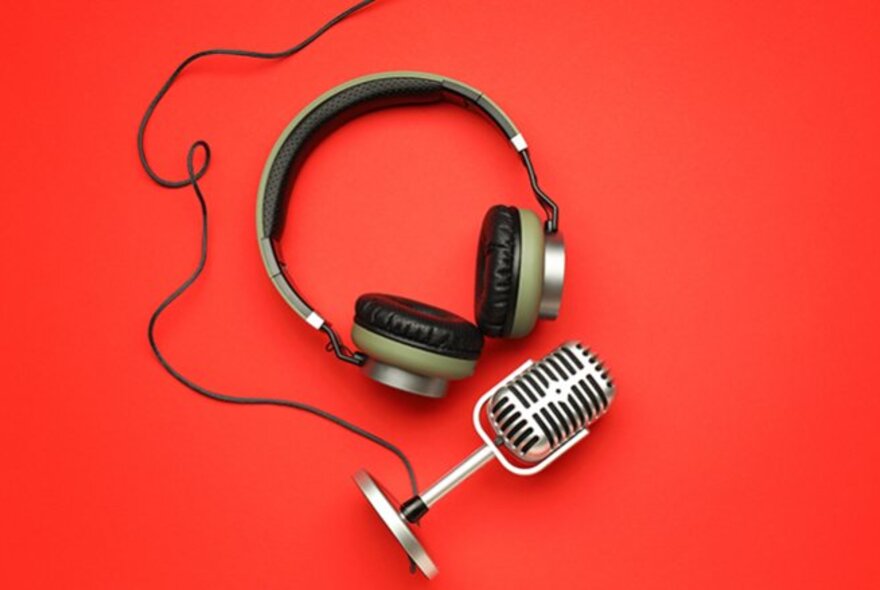 Over-ear headphones and an old fashioned wired microphone, both lying on a red background.