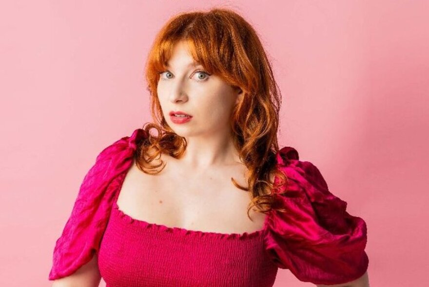 Red-haired woman wearing a pink low-cut dress with short puffy sleeves.