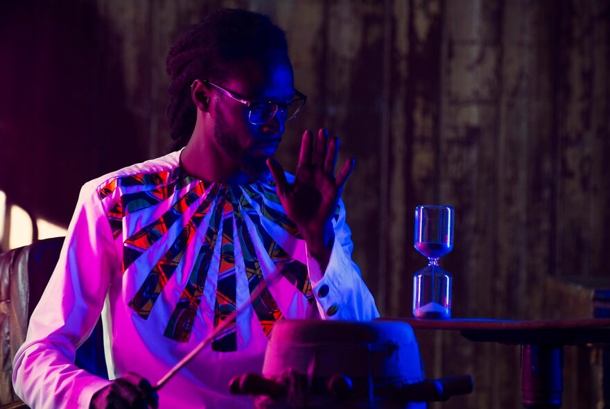 A musician on a darkened stage using a stick to tap a percussive instrument.