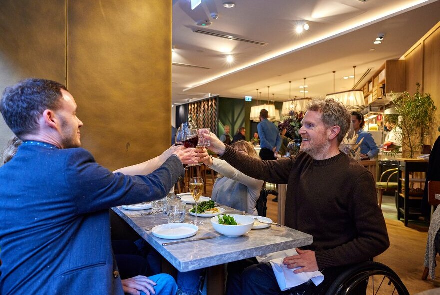 A group of friends are doing a cheers in a restaurant.