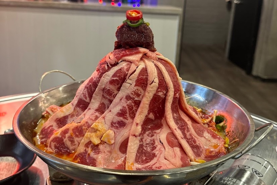 A silver tray of thinly slice raw meat ready to be cooked in a Korean hot pot.