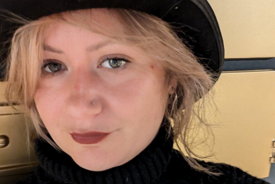A close-up of a woman's face looking perturbed, a black hat cropped out and blonde hair strands around her face. 