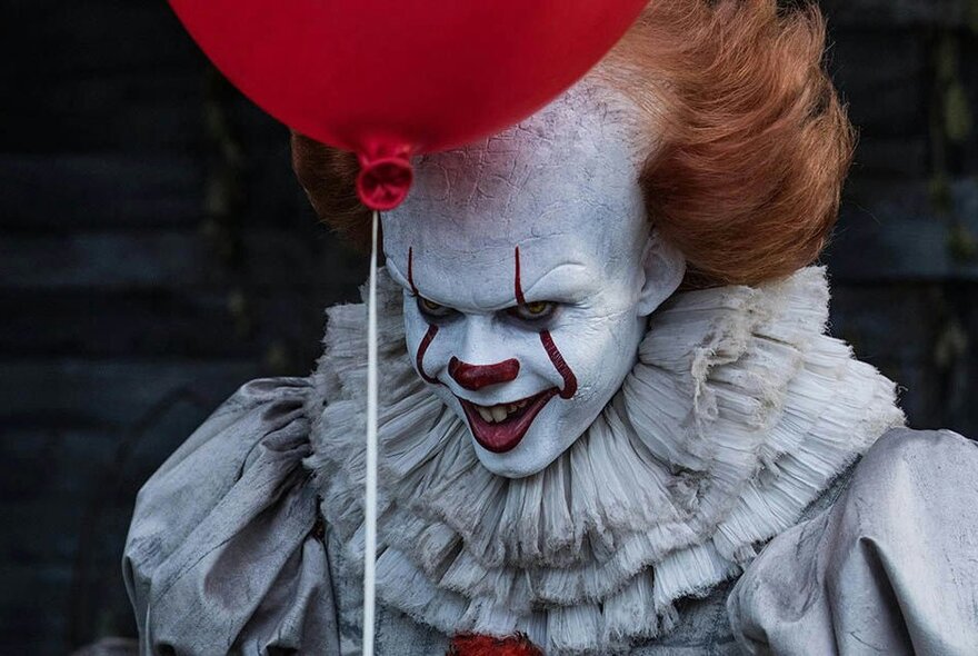 Evil clown character with red balloon in a still from It.