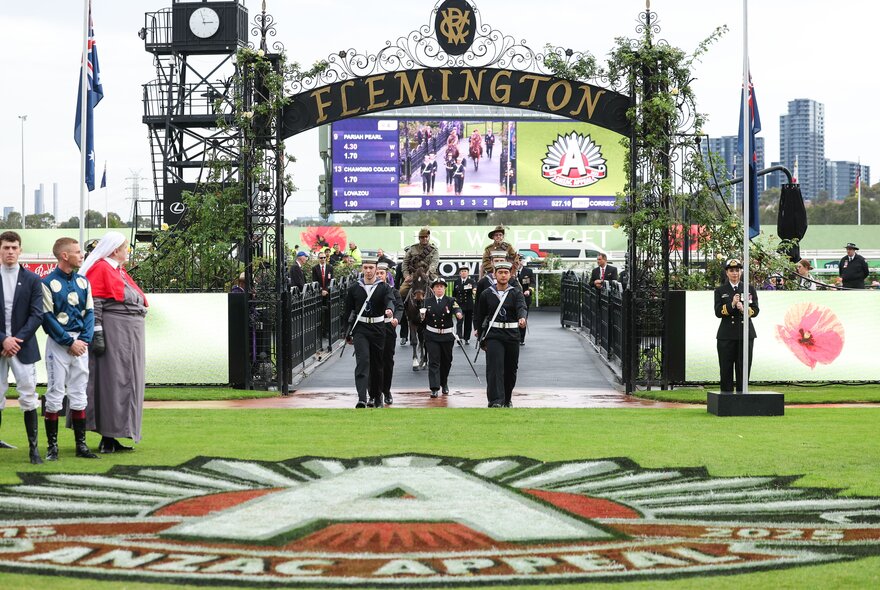 Procession entering Flemington Racecourse under banners to celebrate Anzac Day.