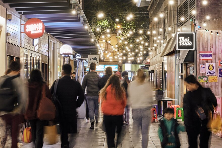 People walking through QV Melbourne's laneways with shop signs and overhead lights.