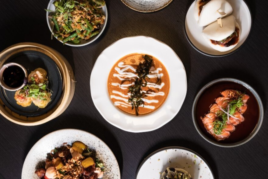 Overhead view of a black dining table in a restaurant filled with several dishes of food.