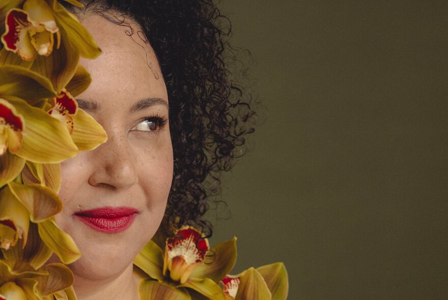 A woman with tightly curled hair peeking out from behind some flowers.