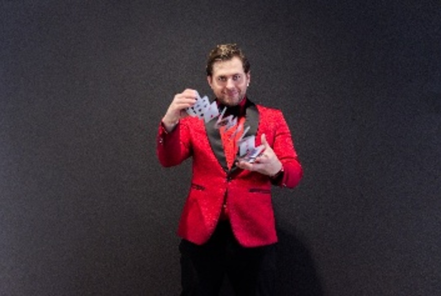 Magician wearing a red and black evening jacket, performing a card deck shuffle.