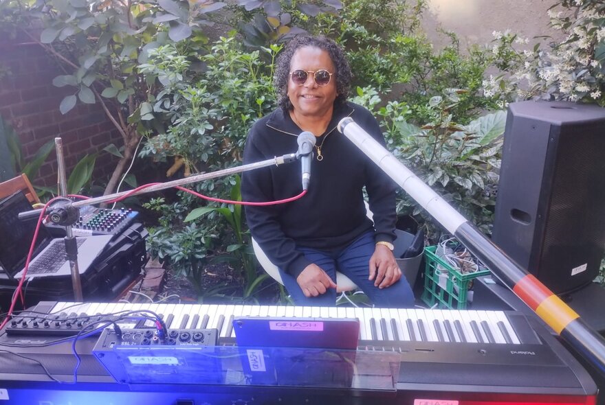 Soul musician Dinash Daniel playing the keyboard in an outdoor setting and smiling broadly. 