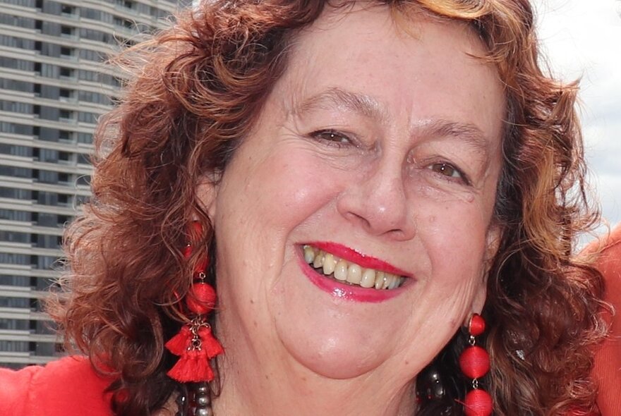 Portrait of historian, Carmel Shute, with red curly hair, red lipstick and long red earings.