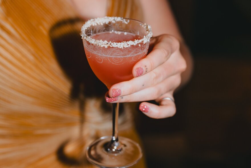 A hand holding a salt-rimmed glass with an orange coloured cocktail.