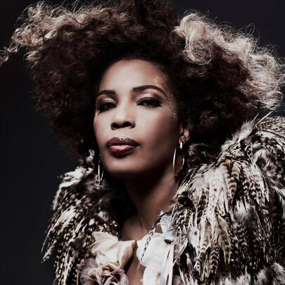 Singer Macy Gray, icily staring at the camera, with an outfit that features feathered shoulders.