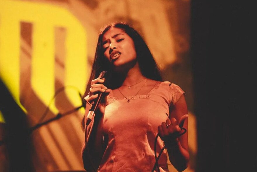 A woman on stage holding a microphone in her hand and singing with her eyes closed.