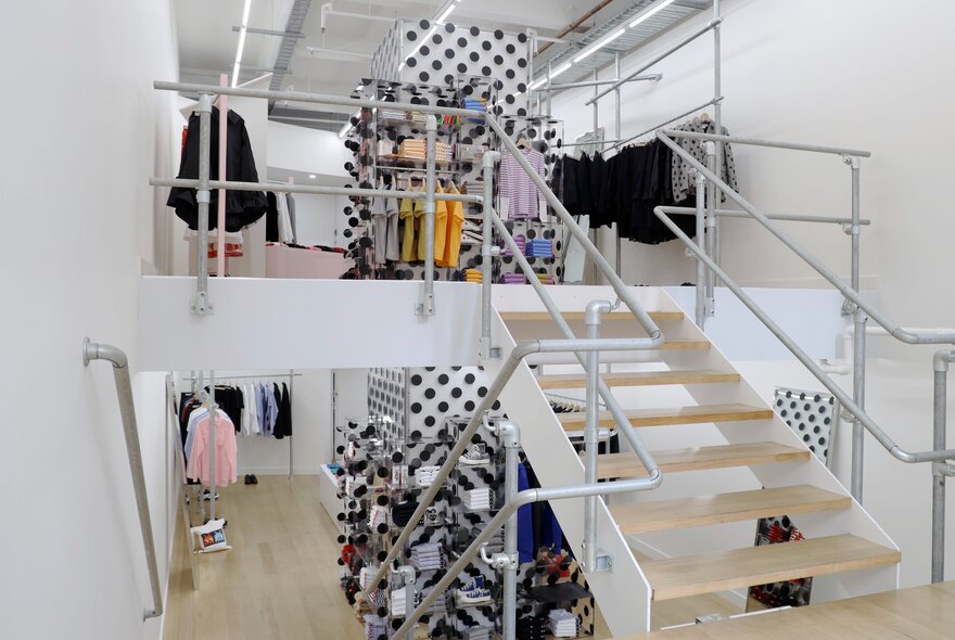 A high-end clothing boutique over two levels, with light wood floors and staircase and black and white polka dots on the walls.