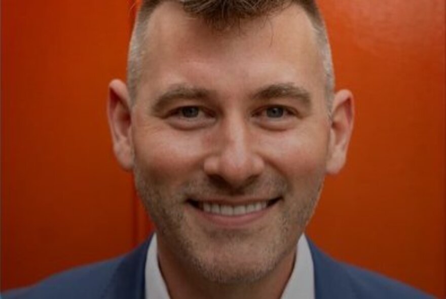 Host of Uncomfortable Conversations, Josh Szeps, smiling; red background.
