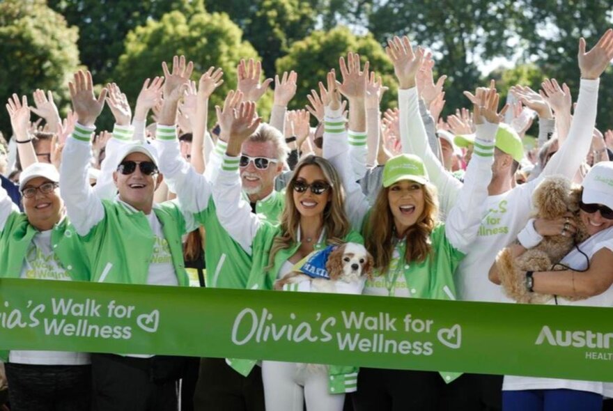 A group of people with their arms in the air, each wearing white and green, behind a large green starting ribbon.