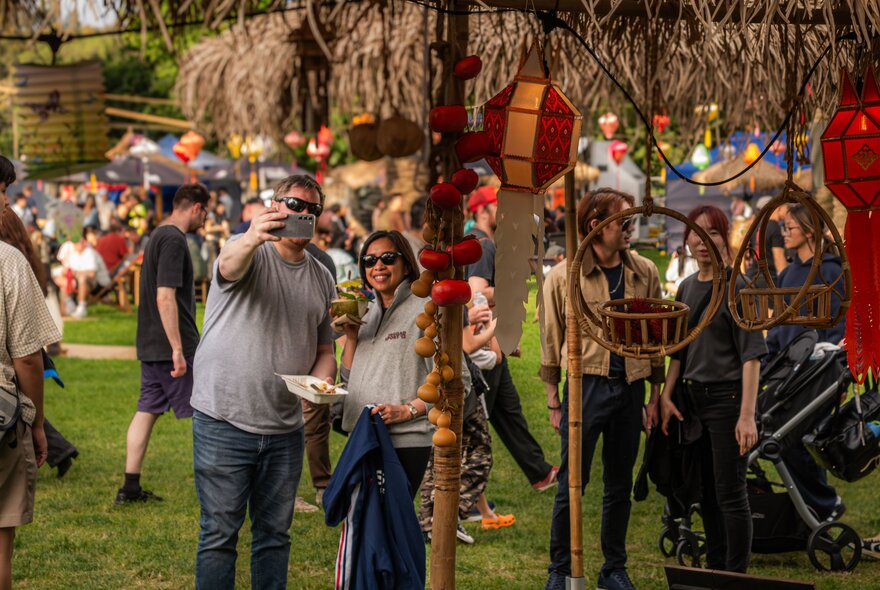 People taking a selfie at an outdoor festival with lanterns.