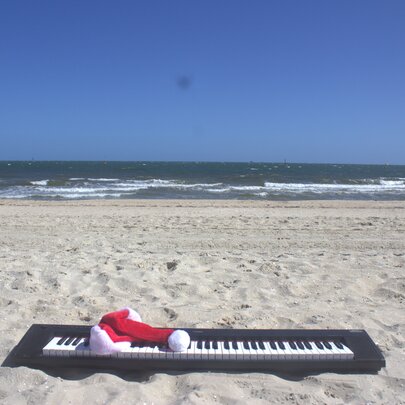 A digital piano keyboard on a beach with a red Christmas hat placed on top of it.