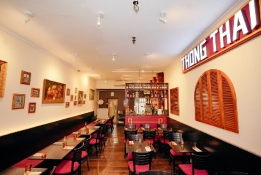 A view of a long restaurant room with tables and chairs leading to the kitchen and bar.