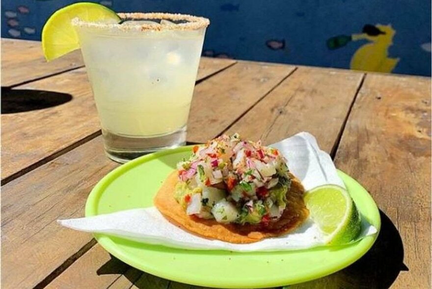 A margarita with salt and lime on a table with a taco.