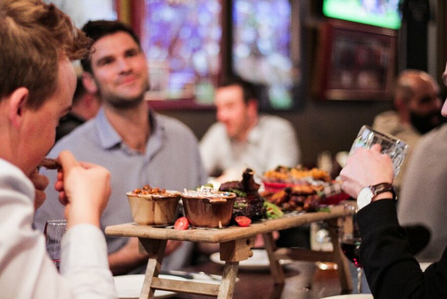 People eating and drinking with an antipasto selection of food on a high tray in the centre of the table.