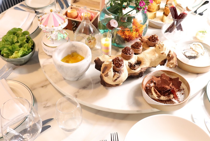 A table setting with a central serving tray with several dishes on a white marble table.