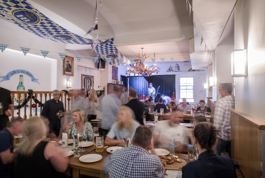 A restaurant dining interior with patrons seated at dining tables, and a band playing in the background on a small stage.