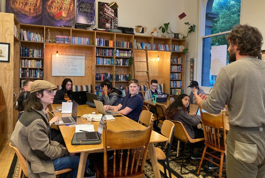 A classroom setting with young people listening to a teacher up the front. 