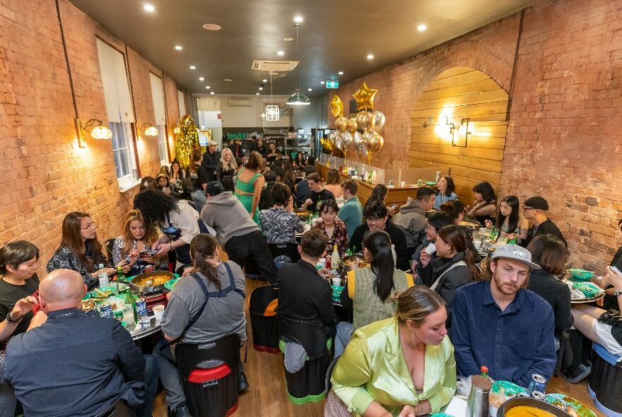 Interior of a crowded restaurant with seated patrons dining at tables, exposed brick walls, and soft ceiling down lights. 