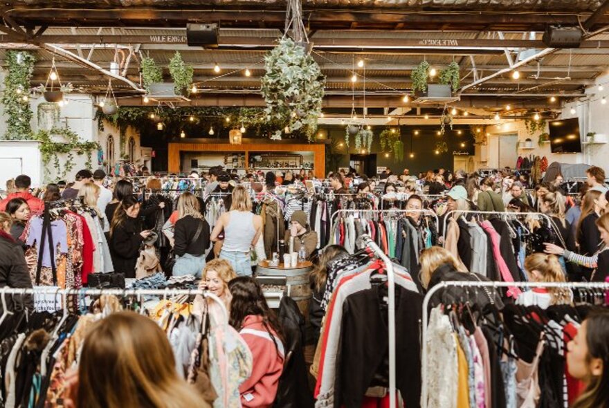 A large room filled with racks and racks of upcycled and pre-loved garments, with people looking through.