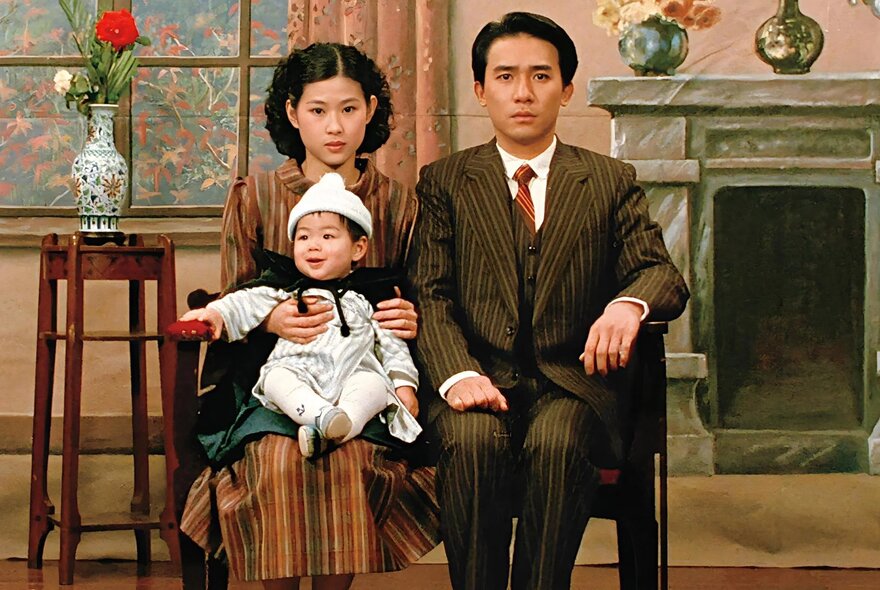 A mid-century coloured photograph of a young Asian family posing formally in front of a set piece designed to look like a wealthy home.