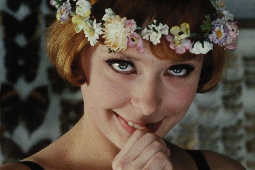 A woman smiling at the camera with her fingers to her mouth, a floral wreath on her head.