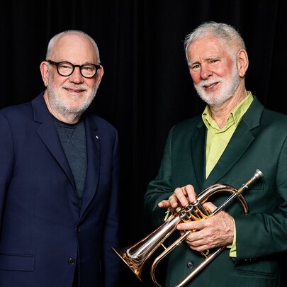 Musicians Paul Grabowsky and Vince Jones (holding a trumpet) smile against a black backdrop.